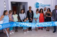 New owner of The Salt Sanctuary of Maryland, LaWanda Stone, is seen using the giant scissors to cut the Grand Opening ribbon. To her immediate left is Chief Executive Officer of the Howard County Economic Development Authority (HCEDA), and to her far right is Howard County Executive Calvin Ball. Stone is surrounded by clients, friends, and family. (Photo provided by Howard County Government)