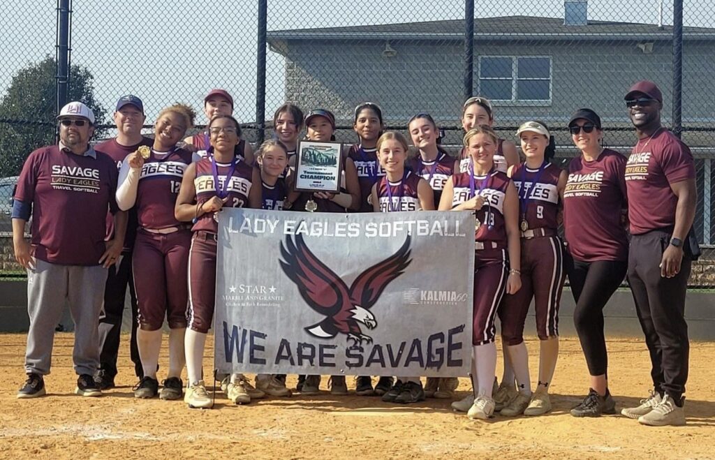 The Savage Lady Eagles, including players and coaches posing on field, holding a banner. All members are dressed in burgundy uniforms (Photo provided by Savage Lady Eagles)